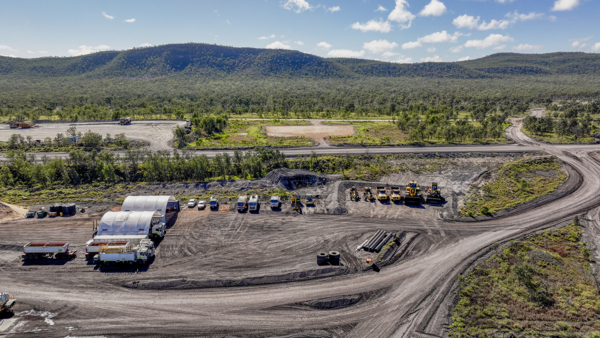 Aerial view of a construction site with machinery and vehicles, set against green hills in Queensland. Aerial view of a construction site with machinery and vehicles, set against green hills in Queensland.